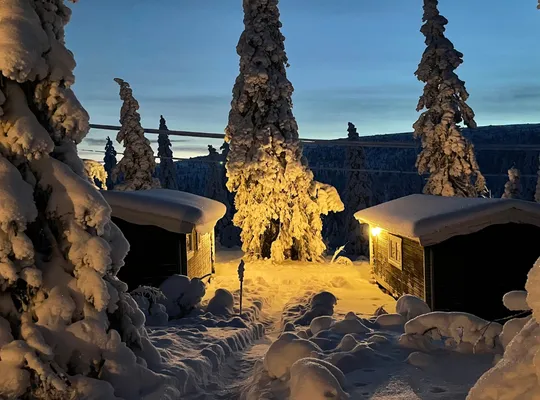 Billedet viser to snedækkede hytter i Sälen, som er oplyst af et hyggeligt, varmt lys.