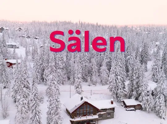 Vinterlandskab med hyggelige hytter og sneklædte skibakker i baggrunden.